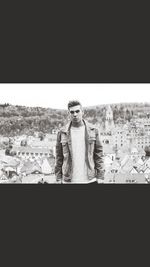 Portrait of young man standing by cityscape against sky