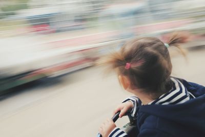 Rear view of girl with pigtails sitting at moving carousel