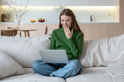 Smiling woman holding laptop on knees, having video call, online communication, web chatting