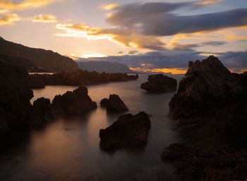 Rocks in sea against sky during sunset