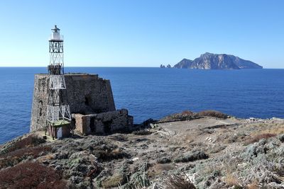 Lighthouse by sea against clear sky