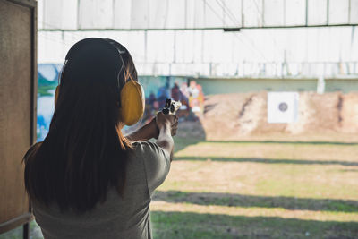 Rear view of woman aiming gun at target shooting range