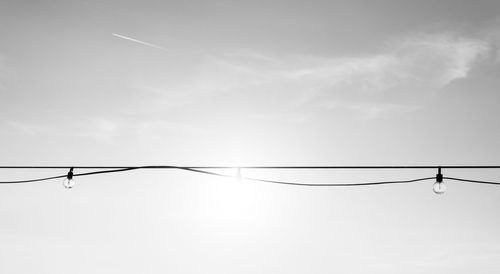 Low angle view of light bulbs hanging on power line against sky