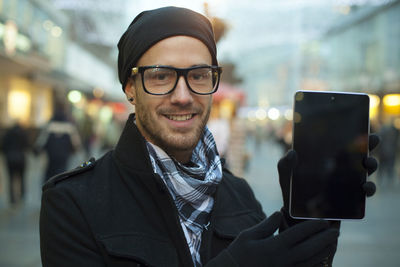 Portrait of smiling man showing digital tablet in city