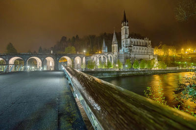 Bridge over river amidst buildings at night