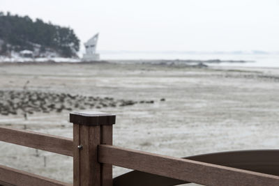 Wooden railing on beach against sky