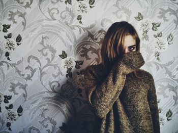 Portrait of woman wearing sweater while standing against designed wall at home