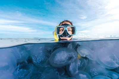 A woman in a black wetsuit is in the water with jellyfish. the jellyfish are floating around her