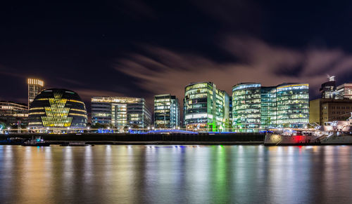 Illuminated city by river against sky at night