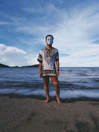 Portrait of young man standing at beach against sky