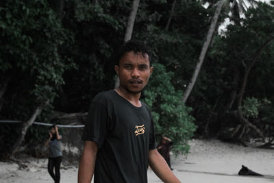 Portrait of young man standing against trees