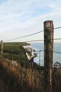 Fence on field by sea against sky