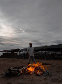 Rear view of man standing by bonfire against sky