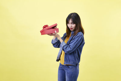 Portrait of smiling young woman standing against yellow background