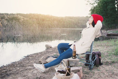 Side view of woman sitting on folding chair by lake