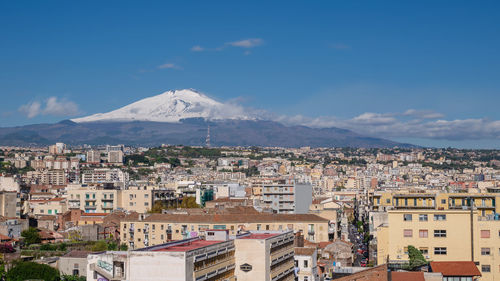 Aerial view of townscape and mountains against blue sky