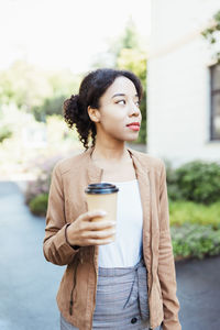 Young african multiracial woman holding disposable paper coffee cup on street