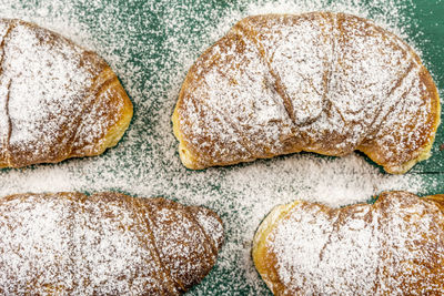 Freshly baked croissants with powdered sugar on a green rustic table ready for breakfast. top view