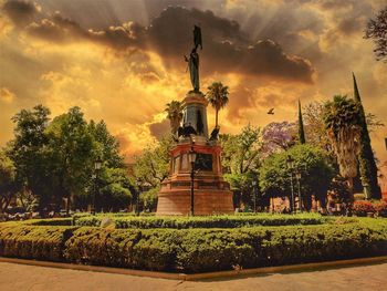 Statue by trees against sky during sunset