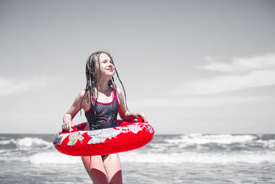 Girl with inflatable ring on beach against sky