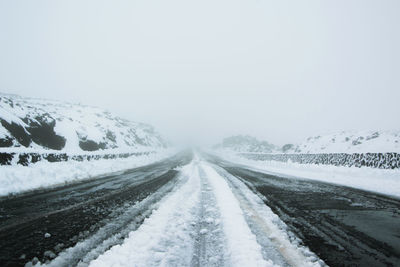 Snow covered road amidst snowcapped landscape against sky