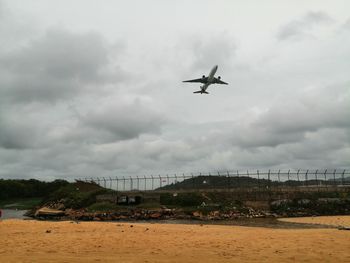 Airplane flying over bridge against sky