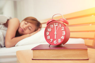 Close-up of alarm clock on book with woman sleeping on bed at home