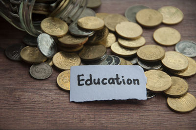 Education text on torn paper with jar, coins and wooden table background. 