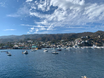 Sailboats in sea by buildings against sky