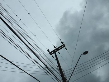 Low angle view of electricity pylon against cloudy sky