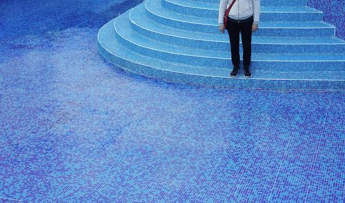Low section of man standing on steps of empty swimming pool