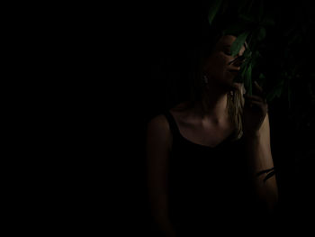 Portrait of young woman standing against black background