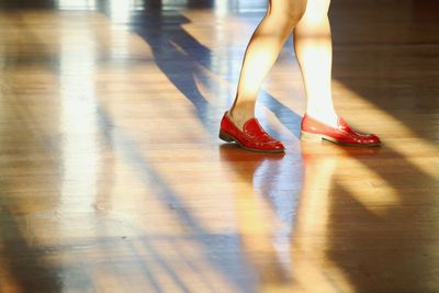 Low section of woman wearing red shoe standing on hardwood floor