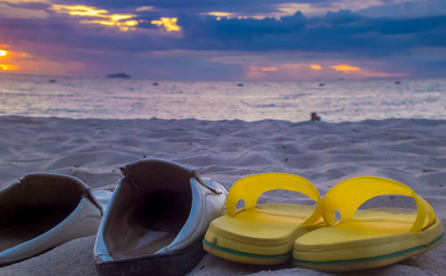 Shoes on beach against sky during sunset