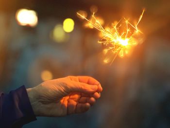 Cropped hand holding sparkler at night