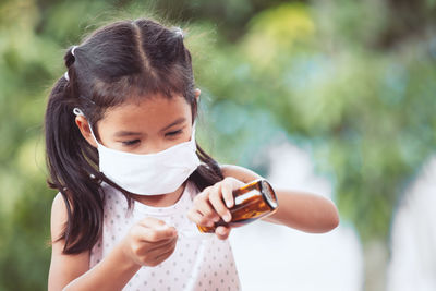 Girl wearing surgical mask while pouring dose in spoon