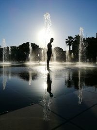 Silhouette man standing by fountain against clear sky