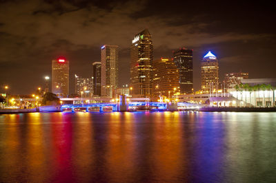 Illuminated buildings by river against sky at night