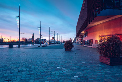 Illuminated street amidst buildings against sky at dusk