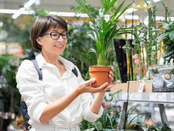 Woman chooses plants for home. shelves with seedlings, flowering plants and seeds in flower shop. 
