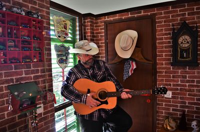 Rear view of a cowboy playing guitar while standing against wall