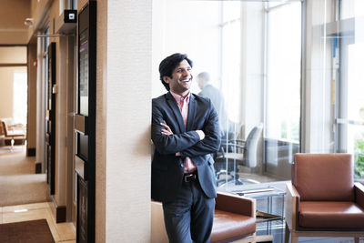 Happy businessman leaning on wall at office