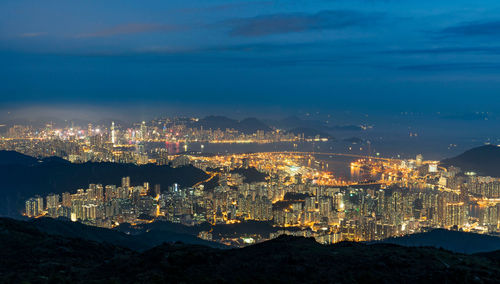 High angle view of illuminated city by sea against sky at night