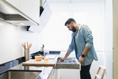 Man cooking in the kitchen in a denim shirt. a man is taking a cutlery