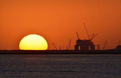 Silhouette cranes against clear sky at sunset