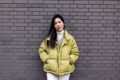 Portrait of beautiful woman standing against brick wall