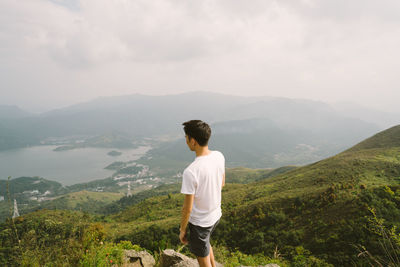 Rear view of man standing on mountain against sky