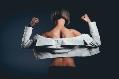 Rear view of seductive woman wearing jacket standing against black background