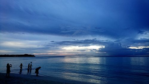 Silhouette people on beach against sky during sunset