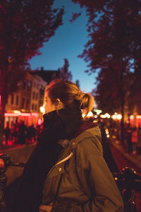 Woman standing by illuminated street at night